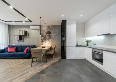 Interior of spacious modern studio apartment with minimalist white furniture in kitchen and comfortable soft sofa in living room